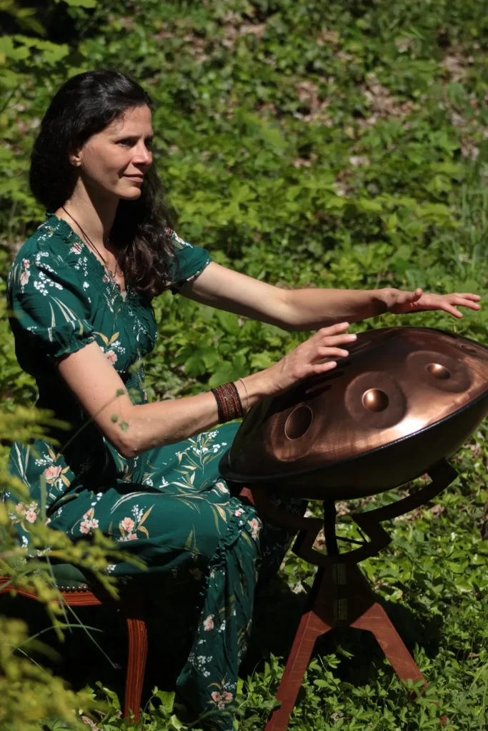 Eine Frau in einem grünen Kleid spielt im Freien inmitten grüner Pflanzen auf einer Handpan.
