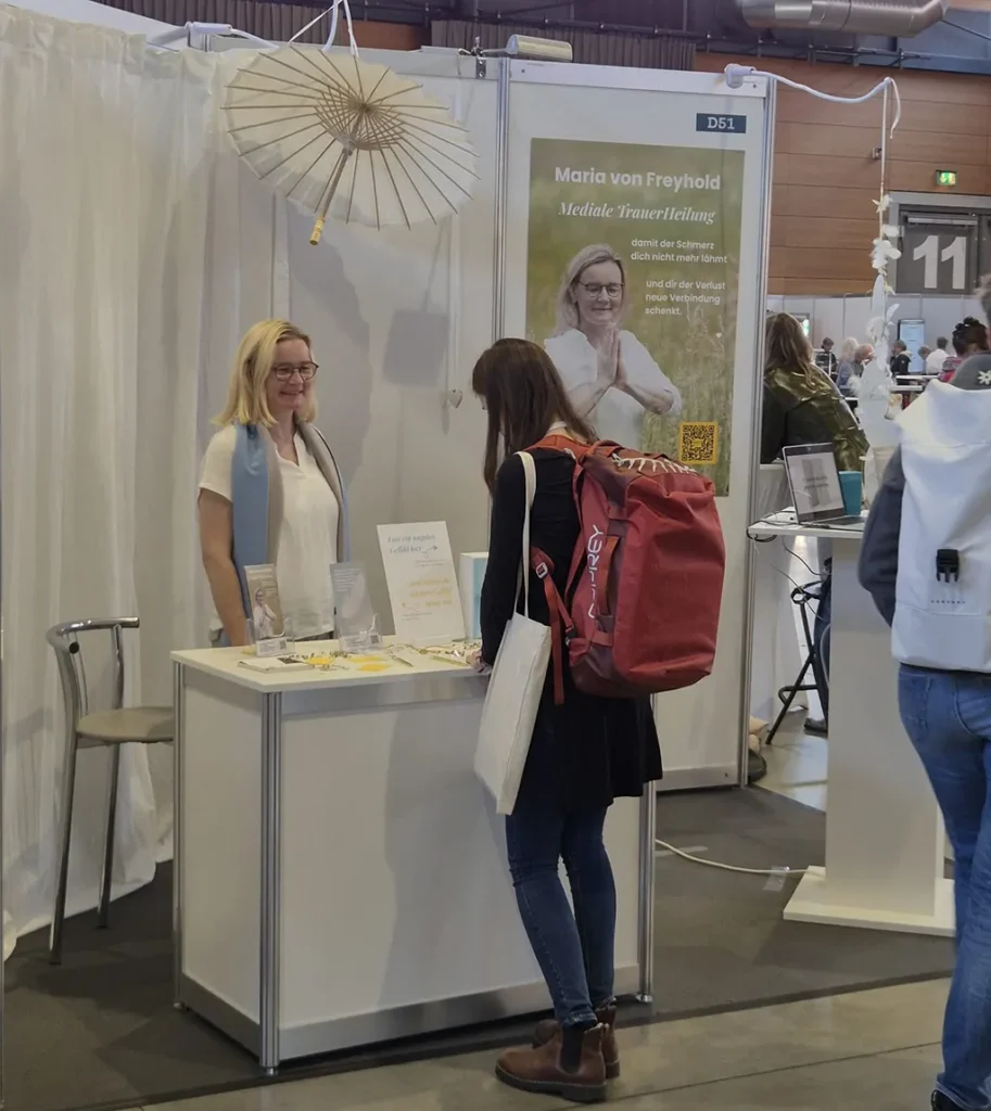 Eine Person mit einem roten Rucksack unterhält sich mit einem Aussteller an einem Messestand.