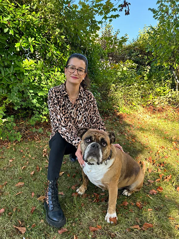 Eine Frau in einem Hemd mit Leopardenmuster, die neben einer englischen Bulldogge kniet.
